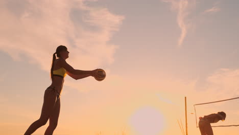 A-beautiful-woman-in-a-bikini-with-a-ball-at-sunset-is-getting-ready-to-do-serve-jump-on-the-beach-in-a-volleyball-match-on-the-sand.-The-decisive-moment-the-tense-moment-of-the-match-in-slow-motion.